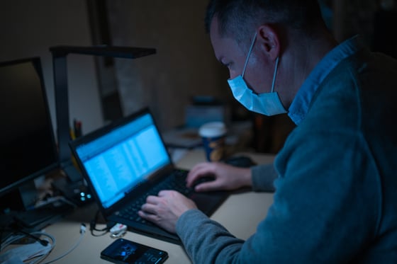 man wearing a hospital mask and typing on a laptop