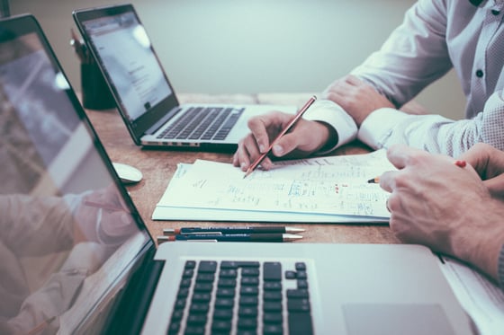 close-up photo of two men reviewing a document in front of two laptops